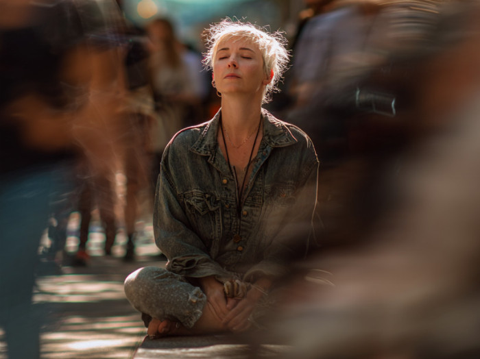 Žena sedí na ulici plné lidí. Chaos, klid.