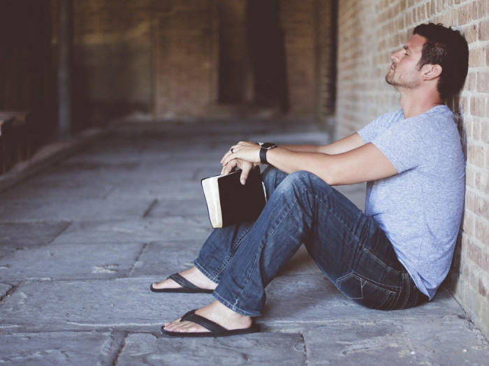 Muž sedí na zemi v kostele a má zavřené oči. V ruce knížku, možná bibli a je v přítomném okamžiku